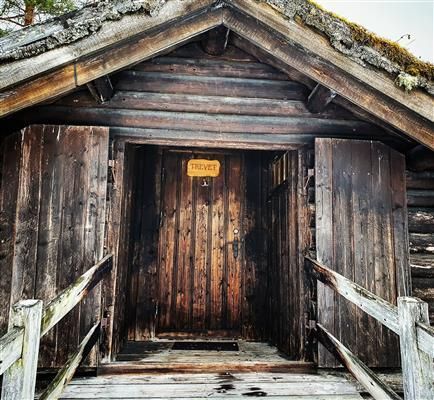 Inngangsparti på tradisjonell hytte med mørkt tømmer og torvtak